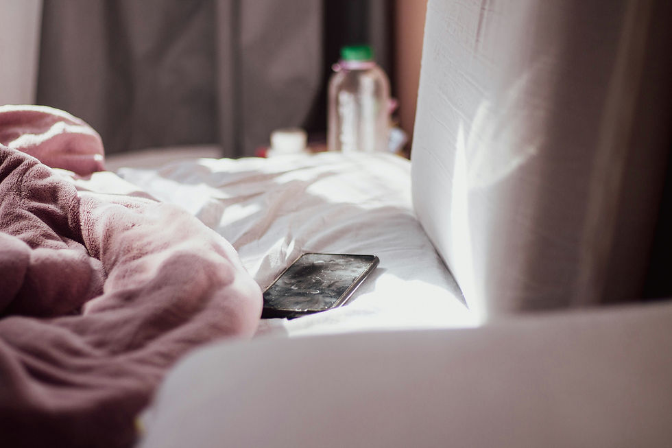 A smartphone on a bed with pink blanket, illuminated by morning light. A water bottle is blurred in the background, creating a cozy mood.