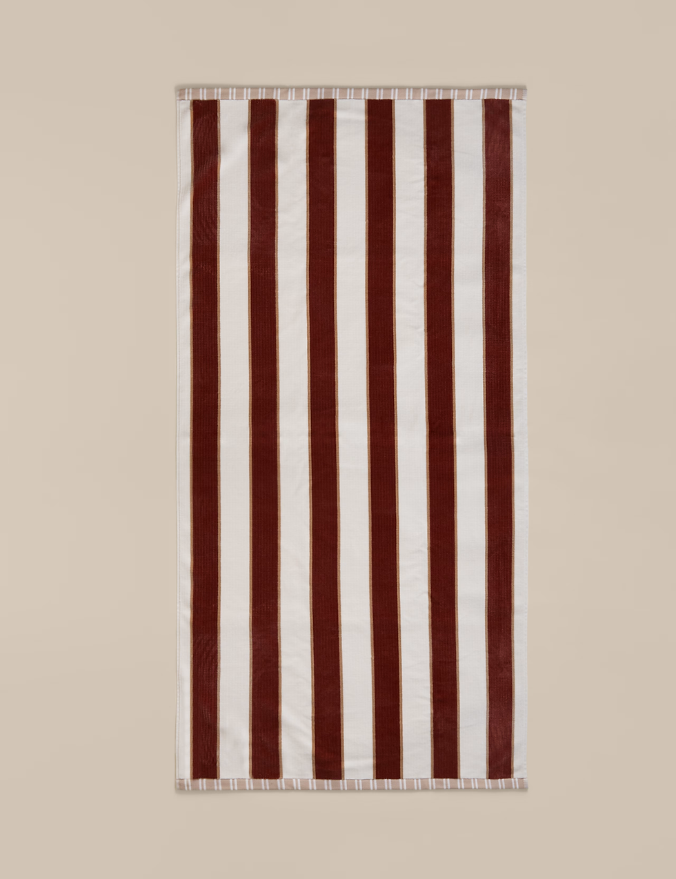 A beige and burgundy striped towel lies flat against a neutral background. The stripes alternate vertically, creating a bold pattern.