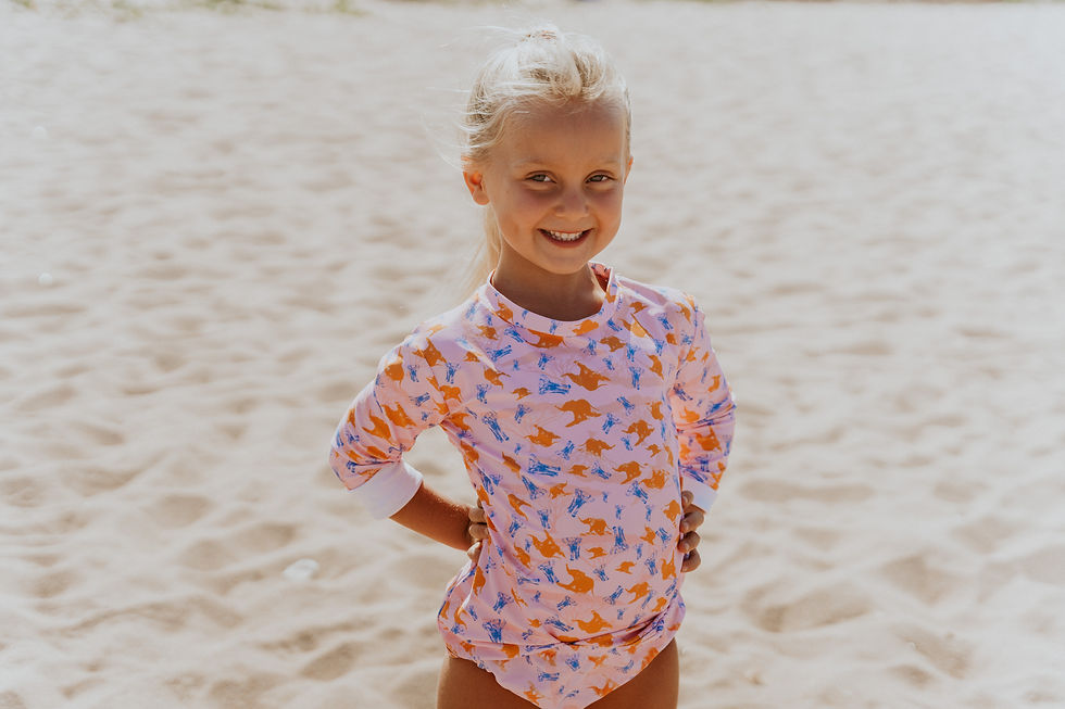 Thumbnail: a girl on the beach in pink elephant printed bikini bottoms and matching rash vest smiling in the sand