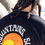 Thumbnail: back view of black crew neck with ocean mountains sunshine emblem on