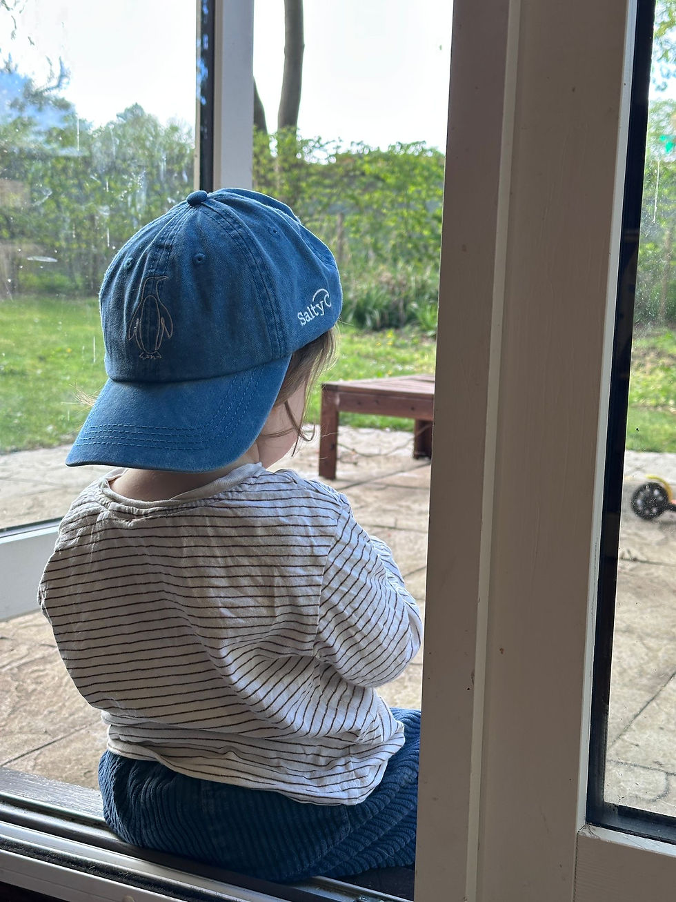 Thumbnail: Turquoise Kids Cap embroidered with a penguin, backwards on a toddler looking out the window