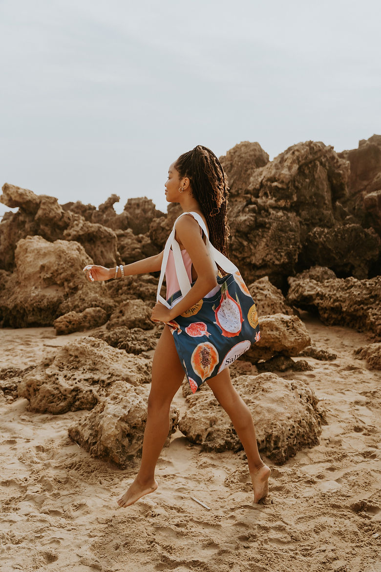 girl floating across the sand in her hannah one-piece and tropical fruits canvas tote bag