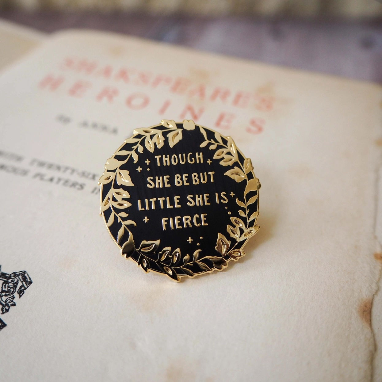 Round black badge with gold detail and words Tho She Be But Little She Is Fierce
