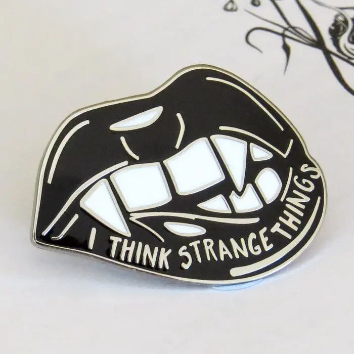 Badge in shape of lips, black lips with white teeth and fangs and words I think strange things