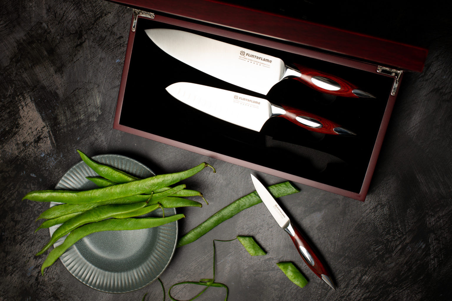 Three Flint & Flam kitchen knives in box with green beans on a plate on table.