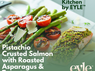 Pistachio crusted salmon served with roasted asparagus and cherry tomatoes on a white ceramic plate with balsamic glaze.