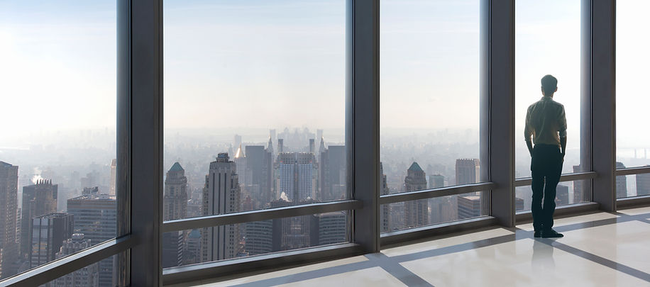Person standing in front of tall windows looking out at buildings of a city