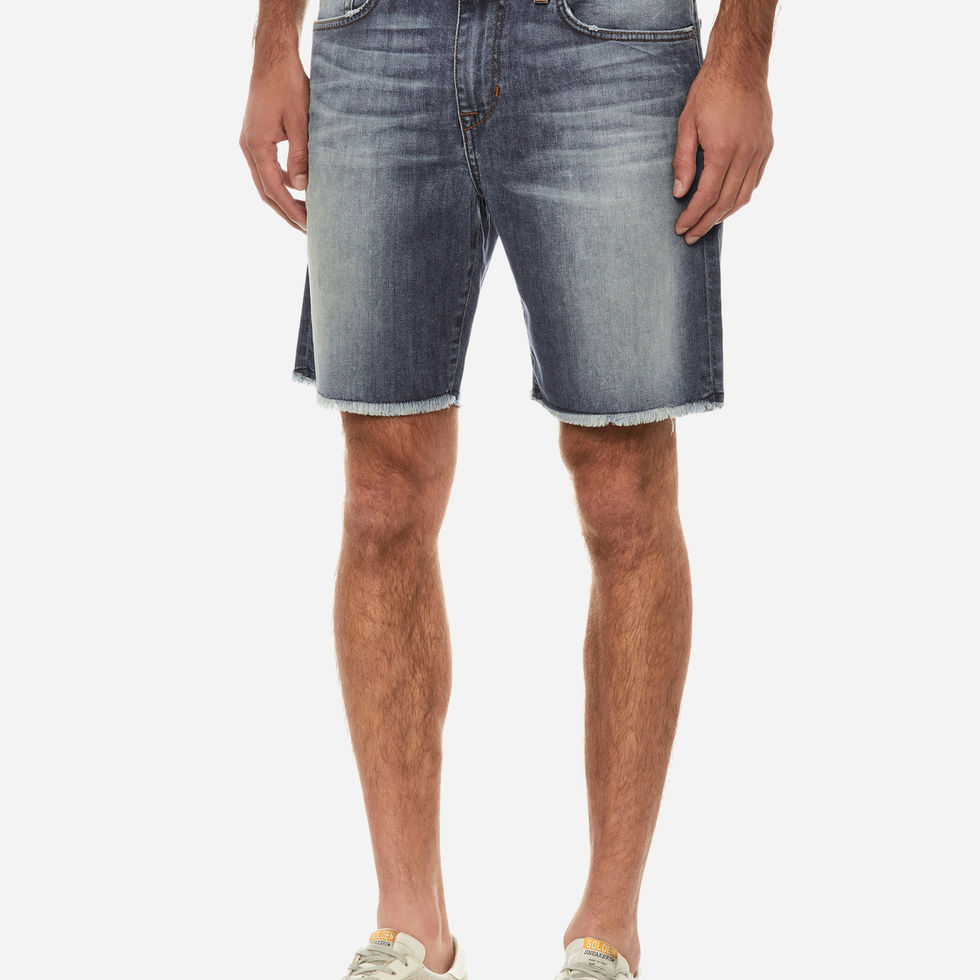 Man wearing distressed denim shorts and white sneakers