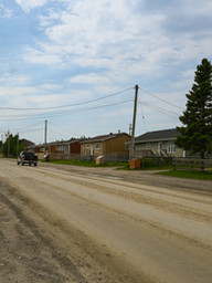 A dirt road with houses on the far side of the street
