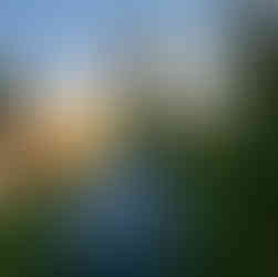 A gret sea to summit tent pitched on grass with trees and a river with the sun rising in the background