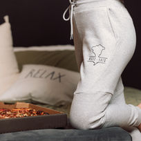 Model wearing gray sweatpants from a streetwear brand, lounging on a bed next to a pizza box.