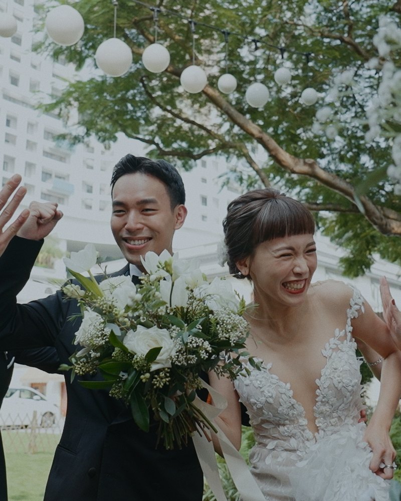 Bride and groom laughing as friends high-five them in a garden