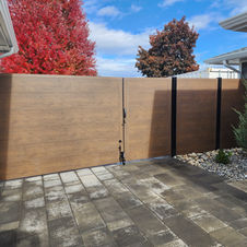 Contemporary wood-tone gate with black fencing in paved backyard patio