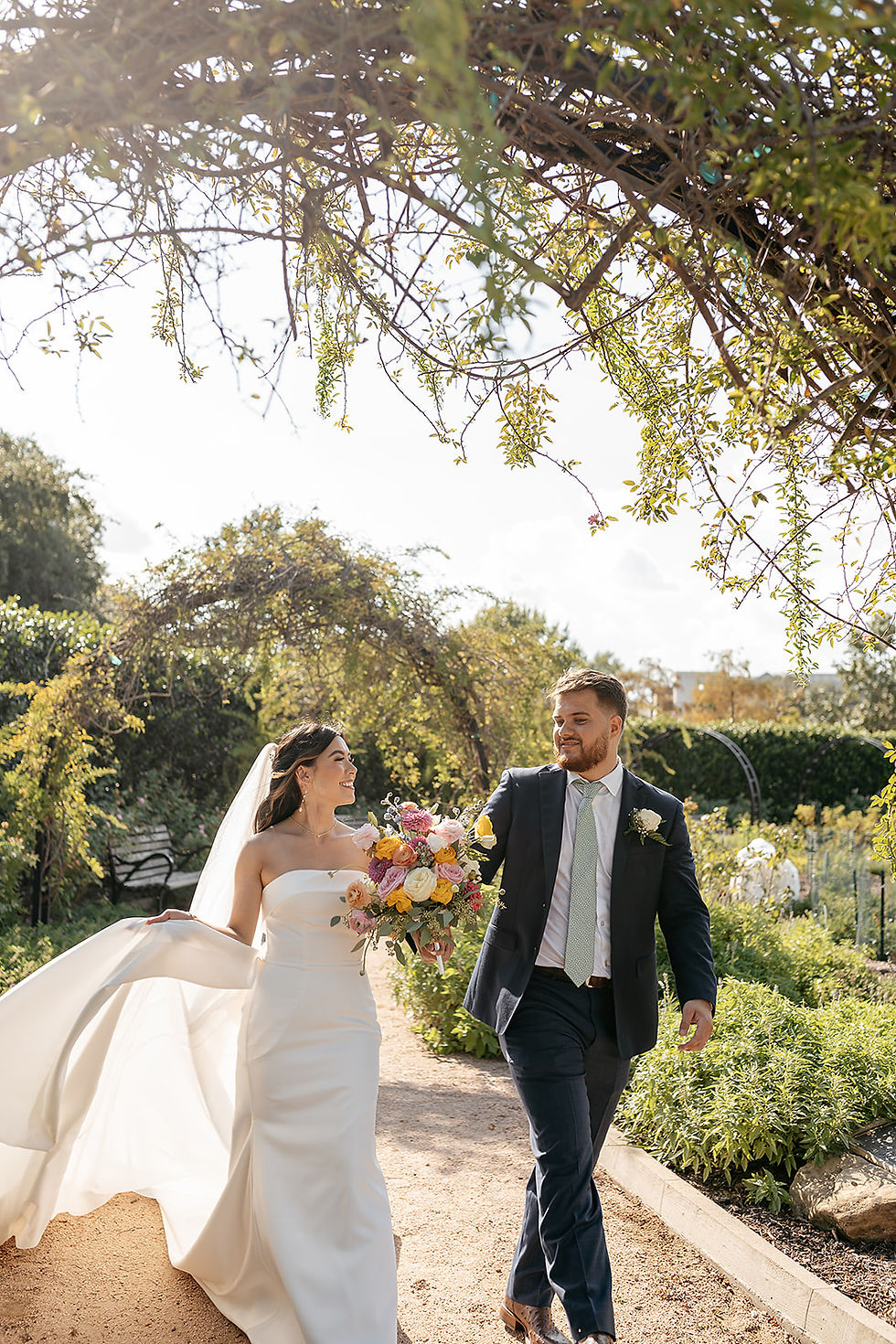 A newlywed bride and groom walking in a park surrounded by greenery