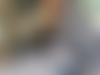 Elderly woman smiling, holding a large blue quilt in The Speedy Bubble Laundromat. Silver dryers in the background, mood is warm and content.