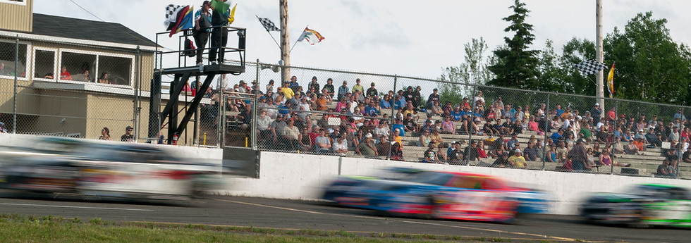 Race cars speeding past cheering fans at a speedway track.