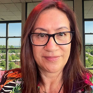 Awhimai Reynolds smiling indoors with large sunlit windows behind her and a bright outdoor view, conveying warmth, approachab