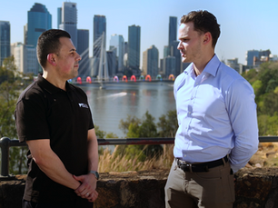 Two real estate professionals in conversation with the Brisbane city skyline in the background.