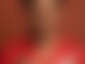 Estelle CHARLERY souriante en blouse rouge écrivant dans un carnet à carreaux Madras, sur fond brun uni.