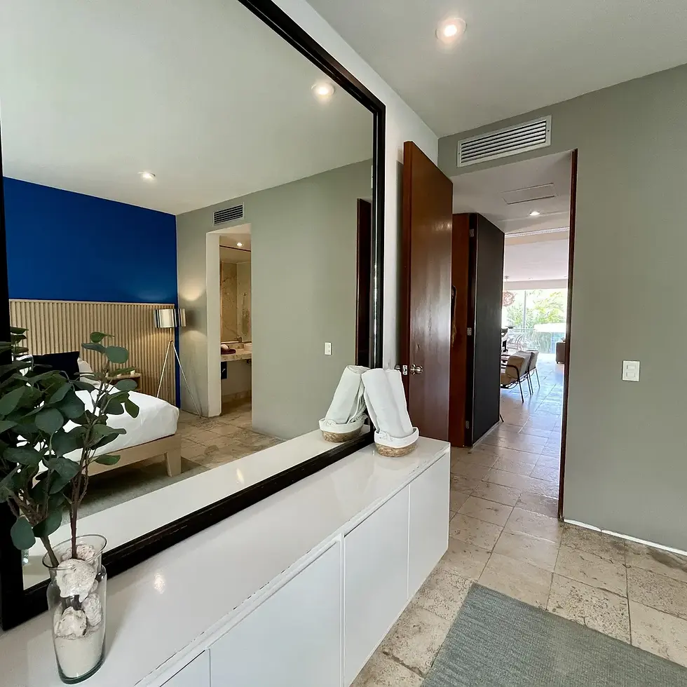 Hallway with large mirror reflecting a bedroom and blue wall