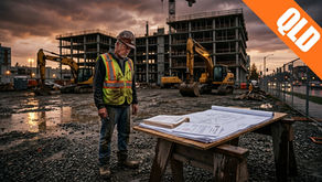 A construction worker in a high-vis vest reviews blueprints at a QLD building site at sunset, with excavators and an unfinished concrete building in the background.
