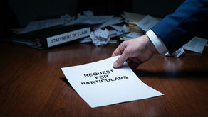 A close-up, slightly high-angle shot showing a person's hand in a blue suit jacket and white shirt cuff placing a white document titled "REQUEST FOR PARTICULARS" onto a polished wooden desk. In the background, slightly out of focus, is a cluttered desk with crumpled papers and a binder labeled "STATEMENT OF CLAIM." The lighting is dramatic and moody, highlighting the document in the foreground.