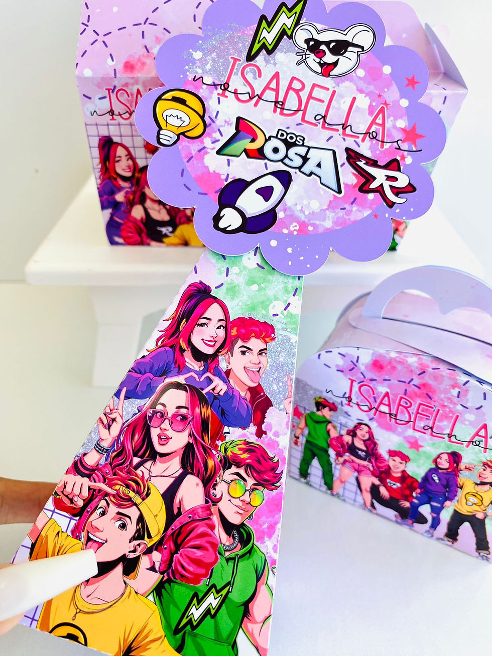 Miniatura: Quatro caixas Dos Rosa personalizadas em lilás e rosa, com ilustrações do grupo, estrelas e topo com logótipo.
