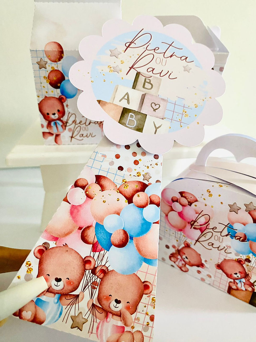 Miniatura: Quatro caixas Chá Revelação personalizadas com nomes, ursinhos, balões rosa e azul, estrelas e cubos com letras.