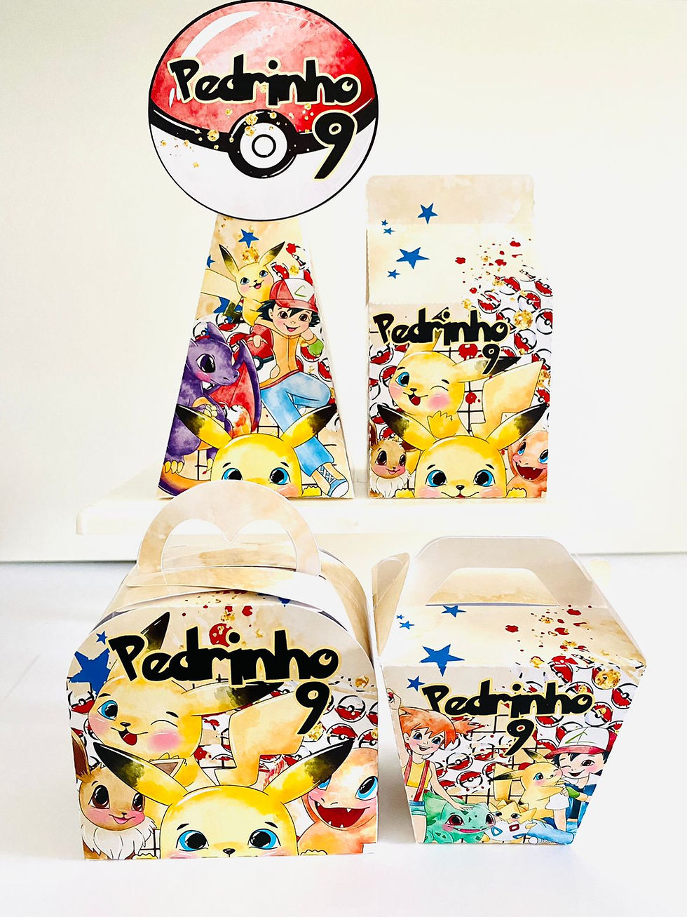 Quatro caixas Pokémon com Pikachu, Ash, estrelas azuis, padrão de Poké Bolas e topo redondo vermelho e branco.