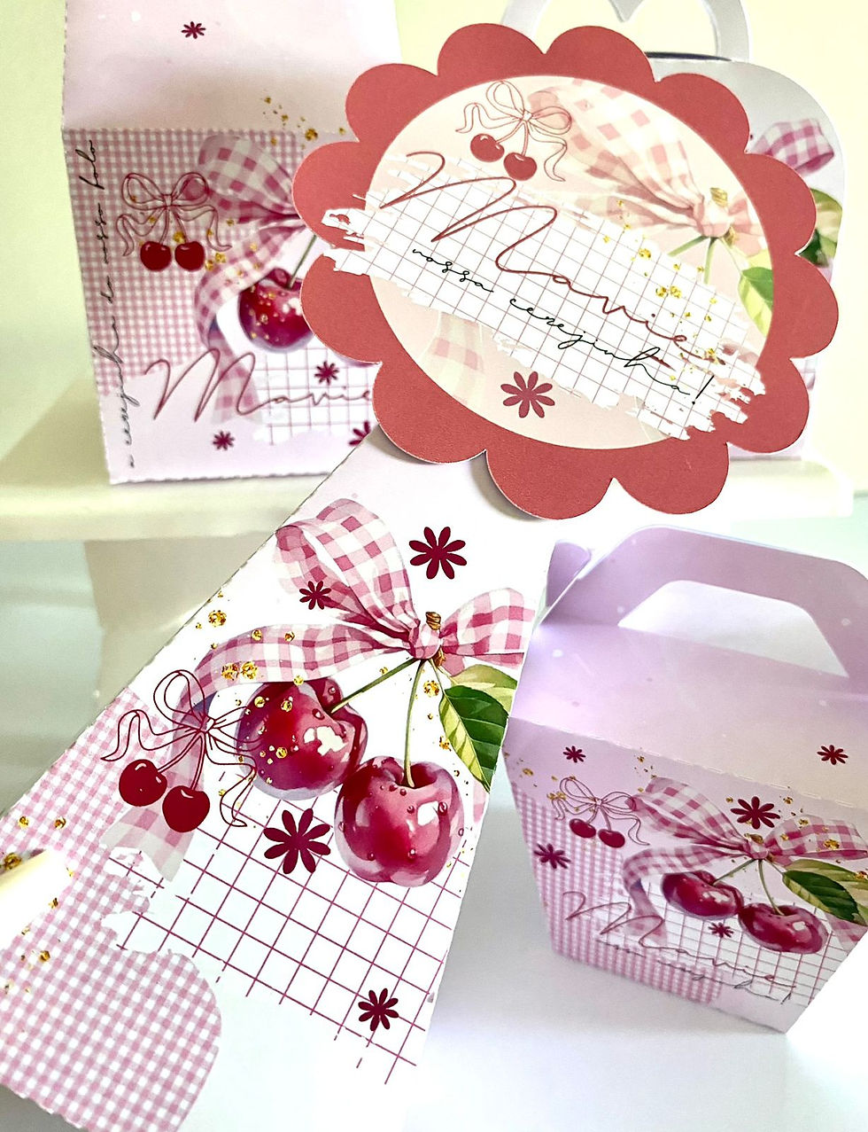 Miniatura: Quatro caixas Cerejinha personalizadas em rosa e branco, com cerejas vermelhas, folhas verdes, laços axadrezados e flores.