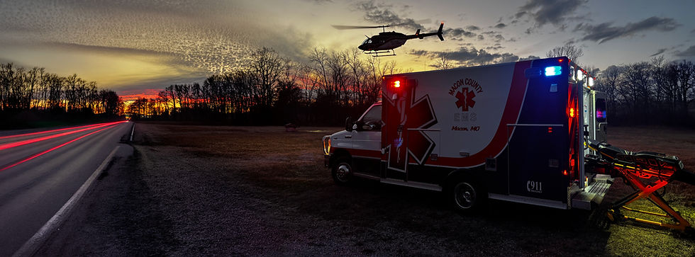 Ambulance with stretcher, flashing lights, and helicopter at dusk