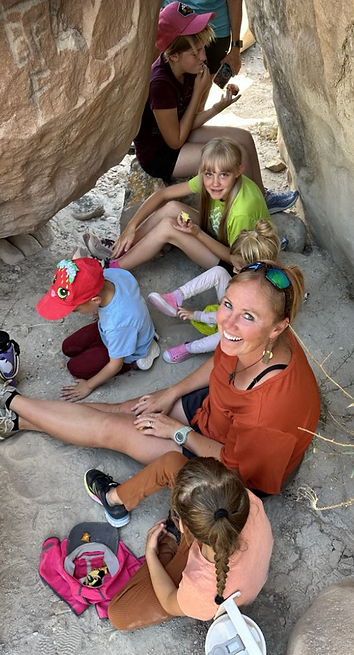 Group of girls and a woman sitting on the ground between two large rocks, Connected Kids Thrive