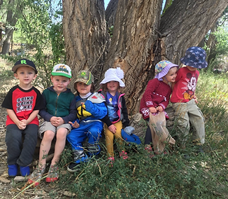Six young children in hats sit together under a large tree.