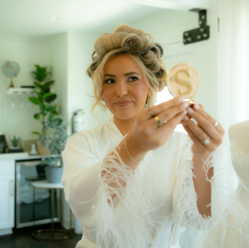 A bride-to-be on the morning of her wedding checking her reflection in a handheld mirror while her hair is in curlers