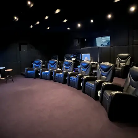 A cozy screening room with plush black recliners, dim lighting, and a small table, perfect for movie viewing.