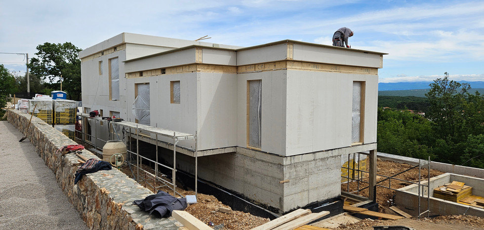 Worker on the roof of a building under construction, white walls, blue sky, mountains.