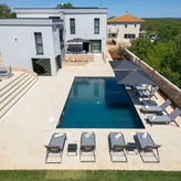 Una casa lussuosa con piscina, lettini prendisole e uno splendido paesaggio verde sullo sfondo.