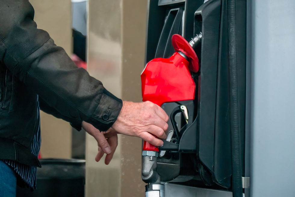 Person in a black jacket refuels a vehicle with a red gas nozzle at a gas station.