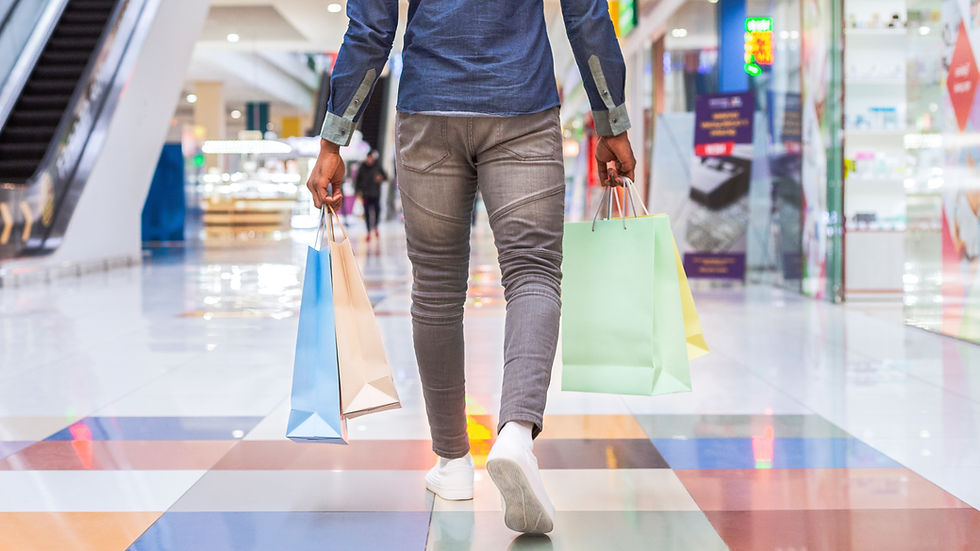 Person walking through a bright mall with colorful shopping bags, seen from behind, with blurred stores and escalators.