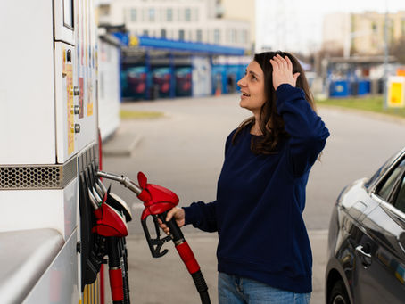 Shocked driver reacting to fuel price on pump while filling car. Woman looking surprised at fuel pump display while refueling car at gas station.