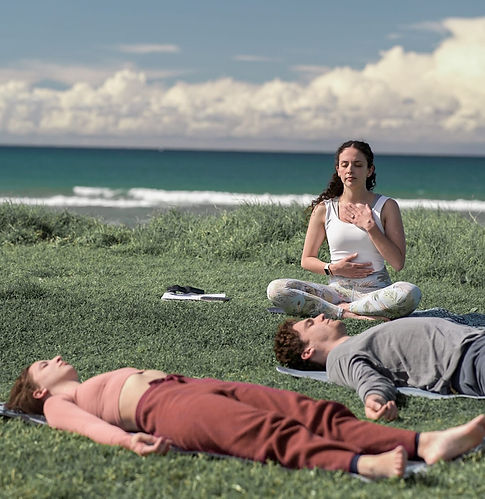 Woman facilitating a meditation session for two people at the beach on the grass