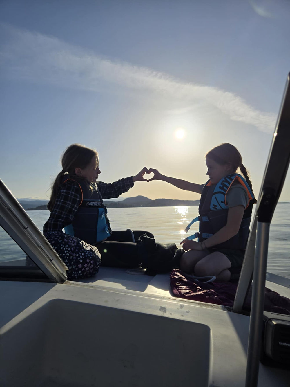 Two people in life vests touching hands on a boat at sunset.