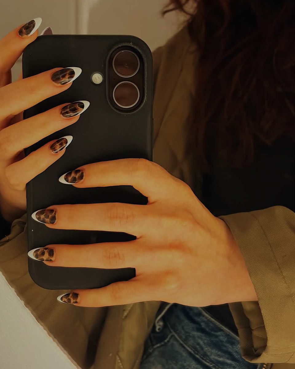 Mãos com francesinha oncinha em unhas amendoadas segurando o celular