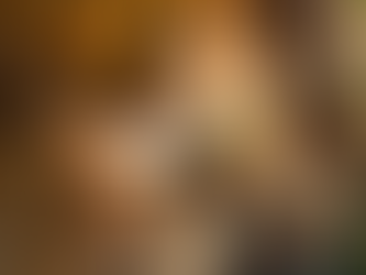 Person in yellow floral top reading a book outdoors on a blanket, with a wicker basket and cup of tea nearby. Relaxed, sunny setting.