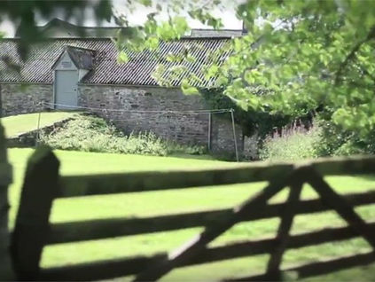 Stone buildings and a garden at the former Auchnagie location, viewed through a gate