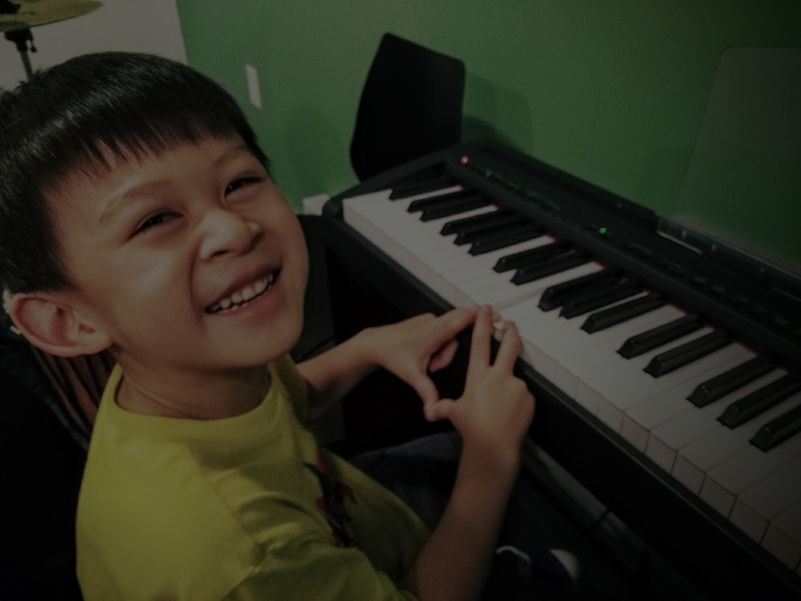 Young boy sitting at keyboard, looking over his shoulder smiling at the camera