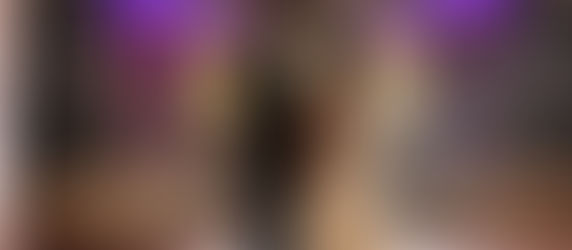 A bride and groom stand in the rain, gazing at each other outside the Riverview Ballroom. The background glows with purple and warm lights.