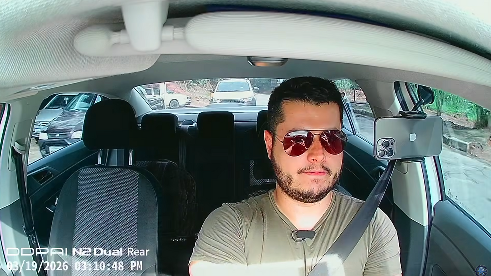 Homem de óculos escuros dirige um carro; interior claro, rua com carros ao fundo e texto da dashcam Câmera Veicular DDPAI N2 Dual no canto.
