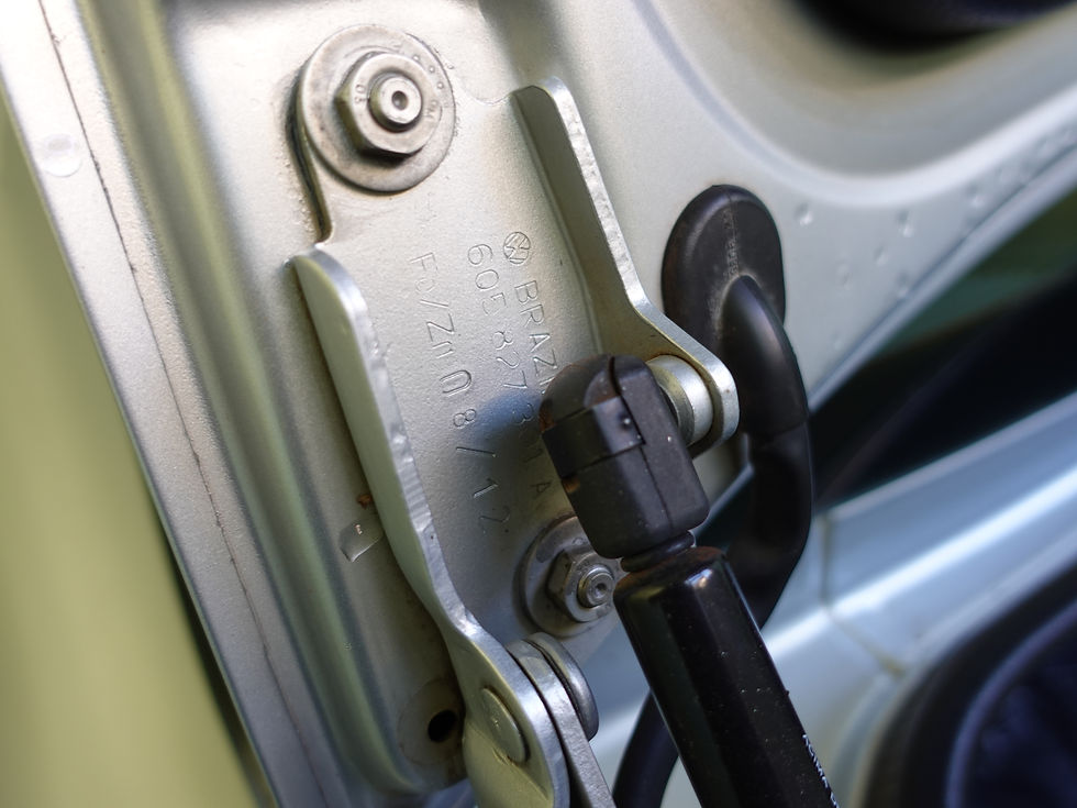 Close-up de uma dobradiça e amortecedor a gás metálicos de carro, com gravação BRAZ, em tons prateado e preto. Como avaliar um carro usado o guia completo.