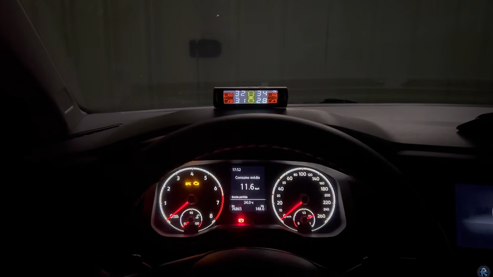 Painel de carro à noite, com velocímetro iluminado e visor mostrando Consumo médio 11,6 km/l e alertas coloridos.